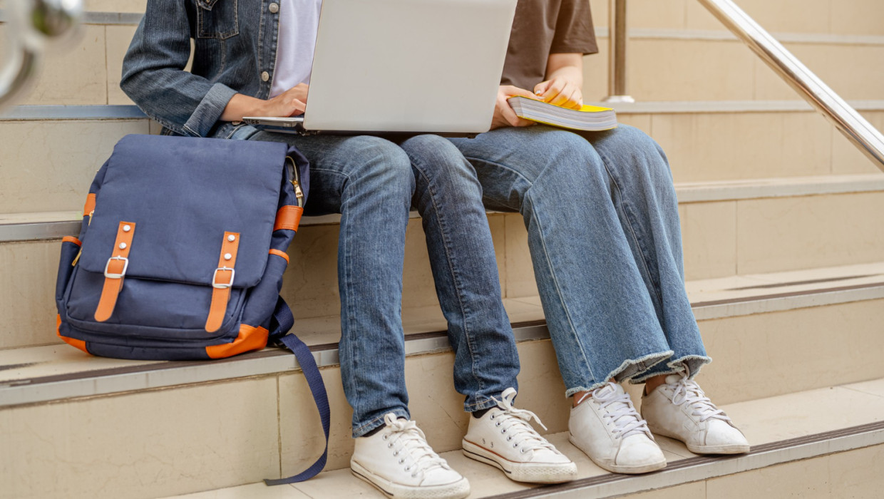 dos estudiantes sentadas en las escaleras usan computadora portátil
