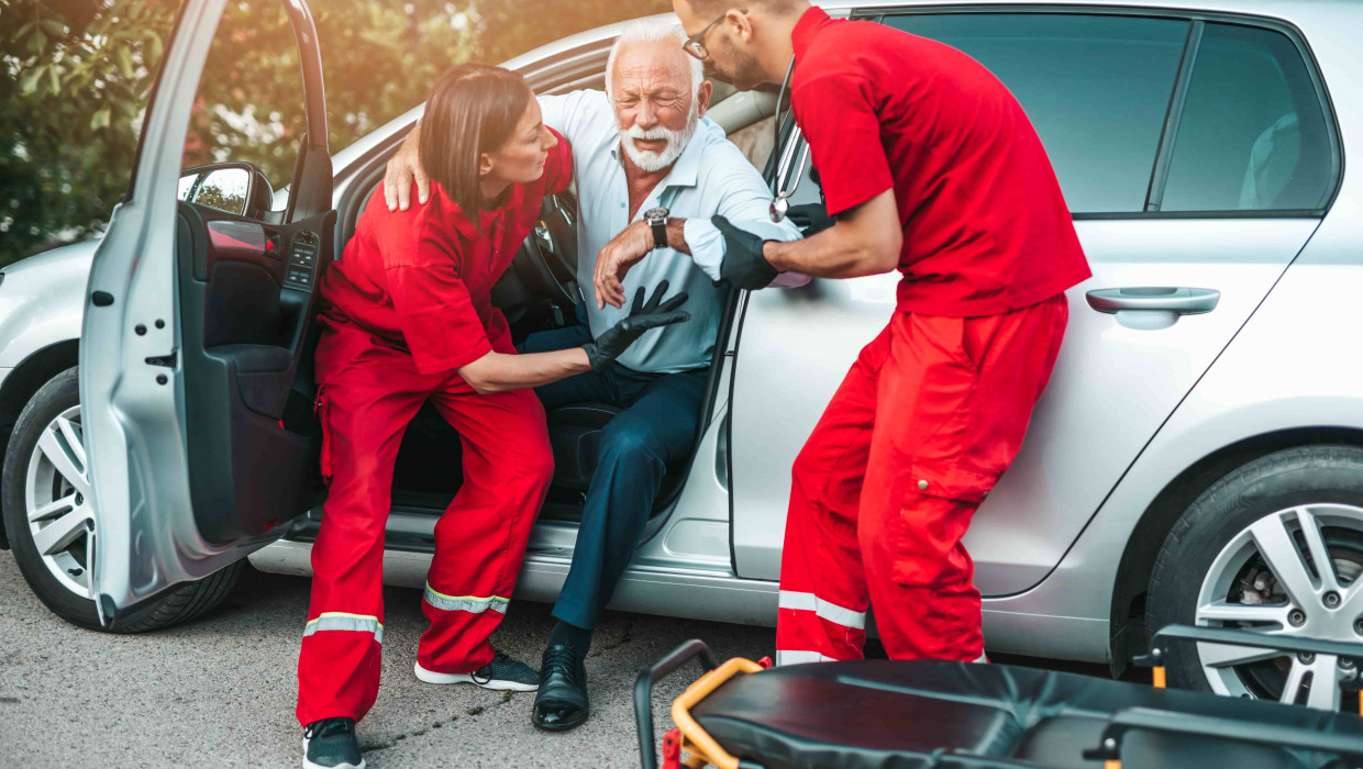 Hombre anciano saliendo del coche ayudado por un equipo médico 