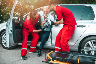 Hombre anciano saliendo del coche ayudado por un equipo médico 