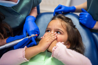 Niña tapándose la boca en el dentista