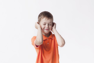 Niño con los ojos cerrados tapándose los oídos