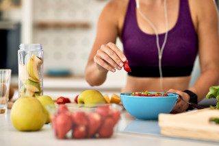 primer plano mujer atletica agregando fresas mientras hace ensalada frutas cocina