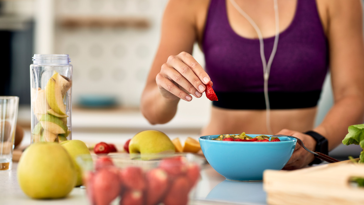 primer plano mujer atletica agregando fresas mientras hace ensalada frutas cocina